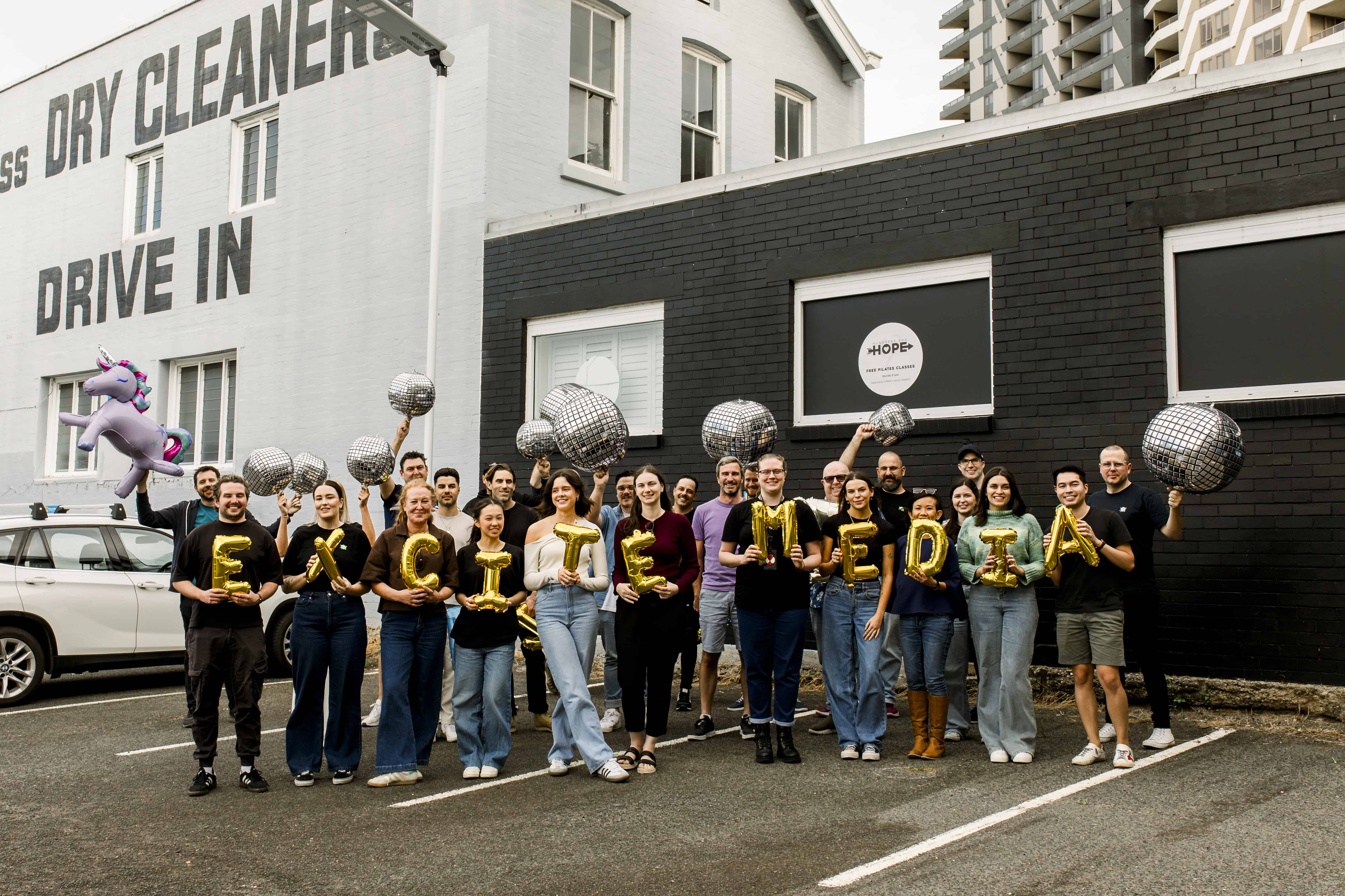 The Excite Media team holding gold foil balloons that spell 'Excite Media'