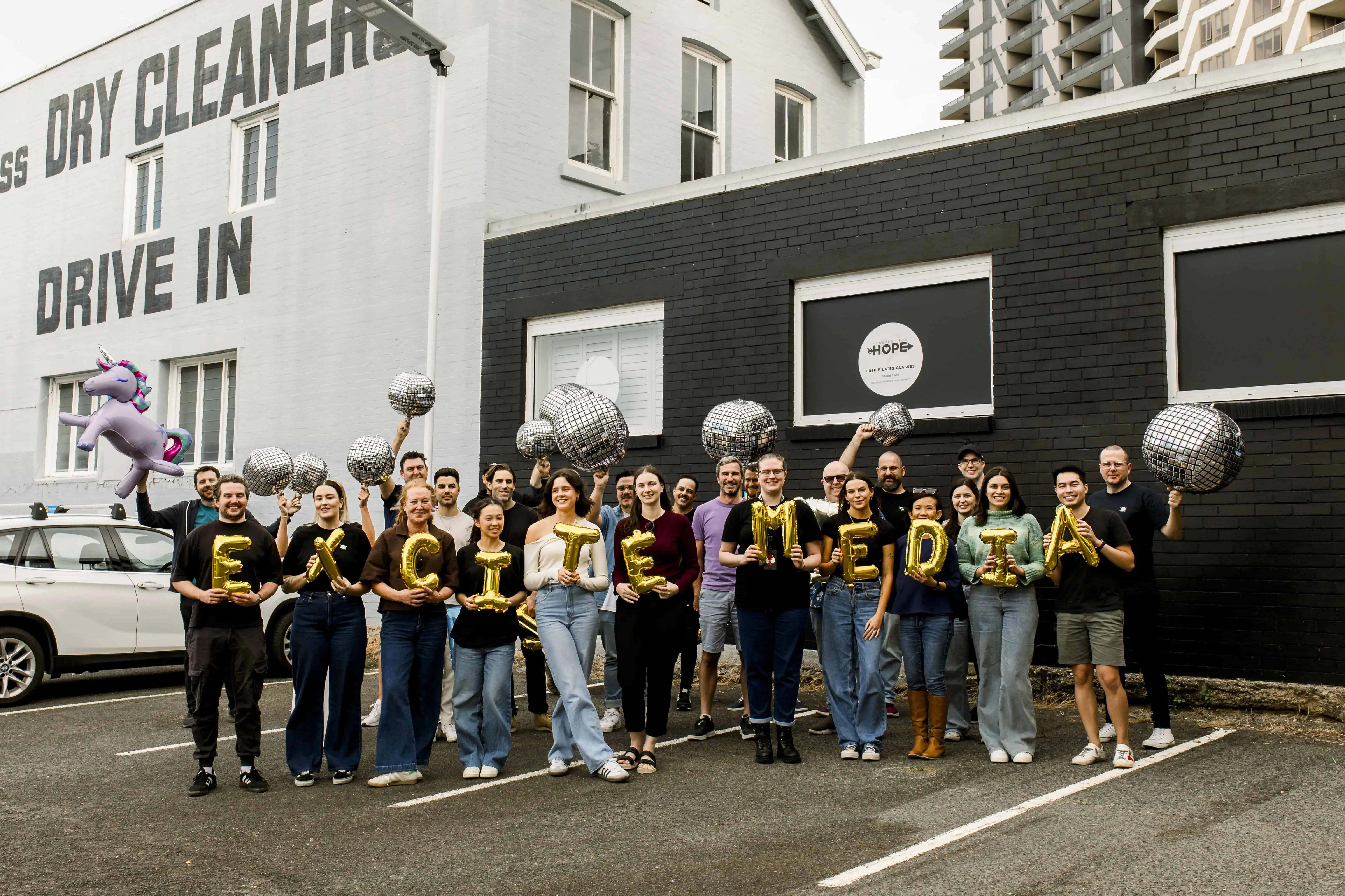 The Excite Media team holding gold foil balloons that spell 'Excite Media'