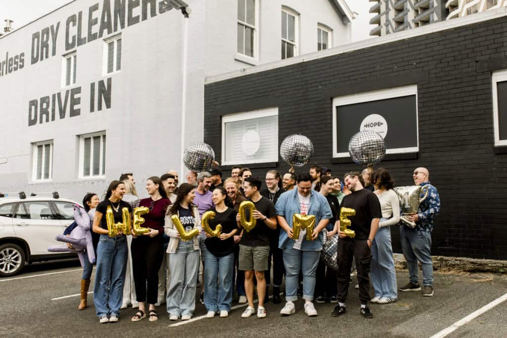 Excite Media team holding gold foil balloons in a car park that read 'welcome'
