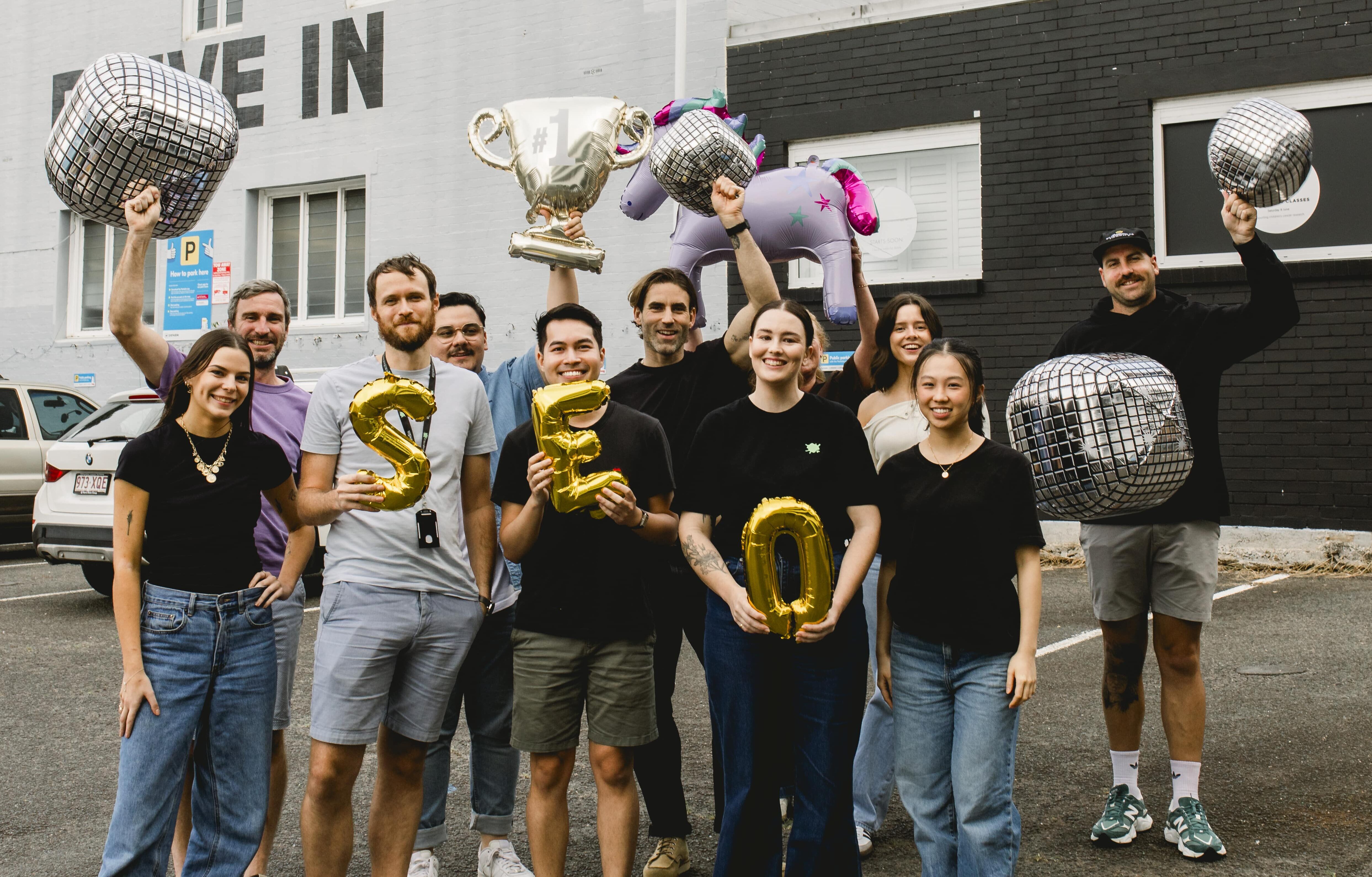 SEO team standing in a car park holding an assortment of balloons, including letters that spell SEO