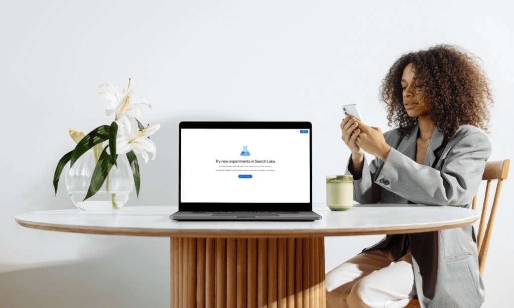 black woman near the table holds phone beside a laptop