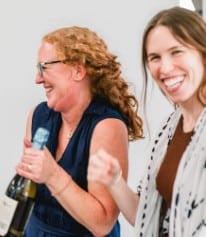Jess Childs smiling and holding a champagne bottle next to a colleague